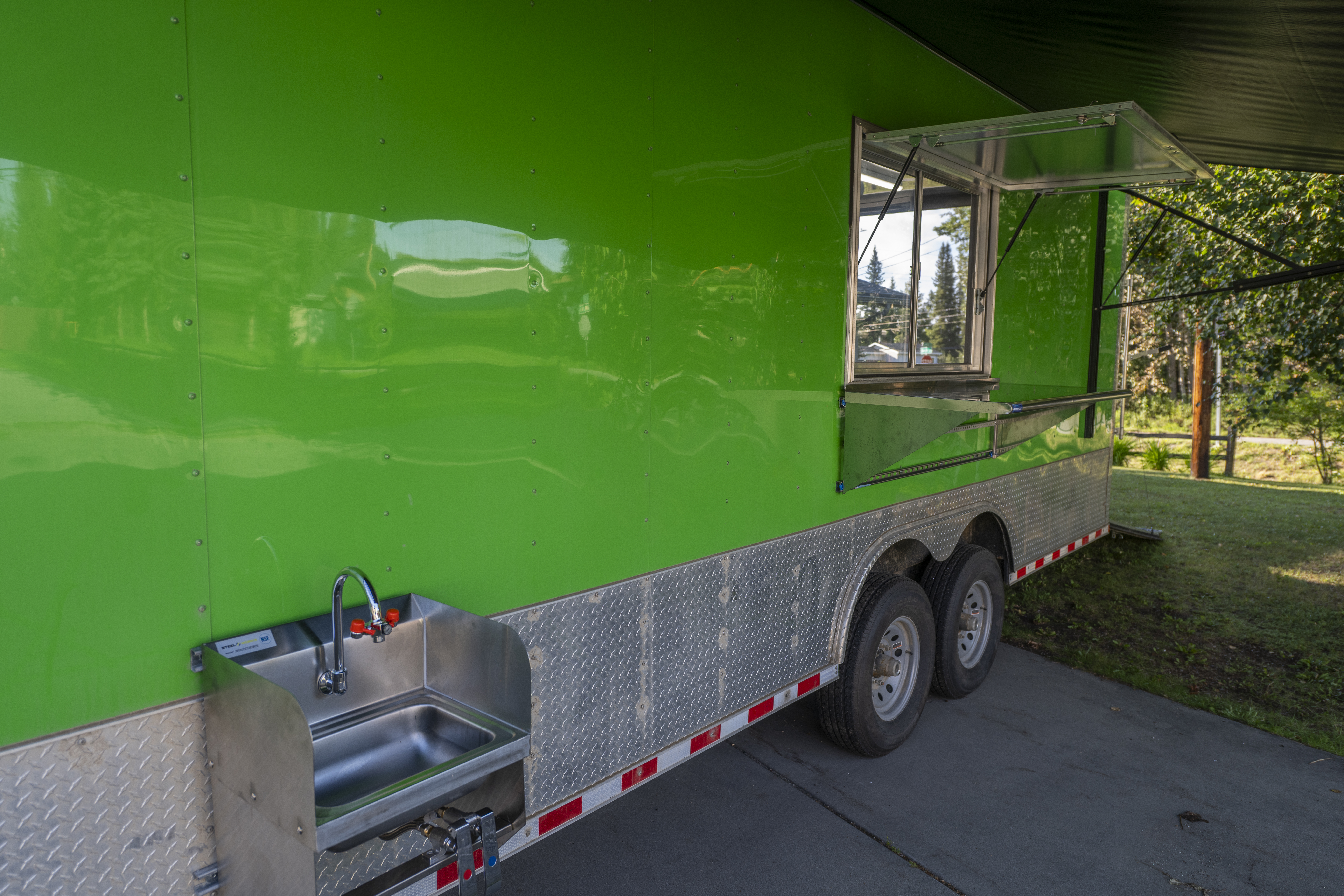 Exterior of the green mobile kitchen trailer with an awning and service platform