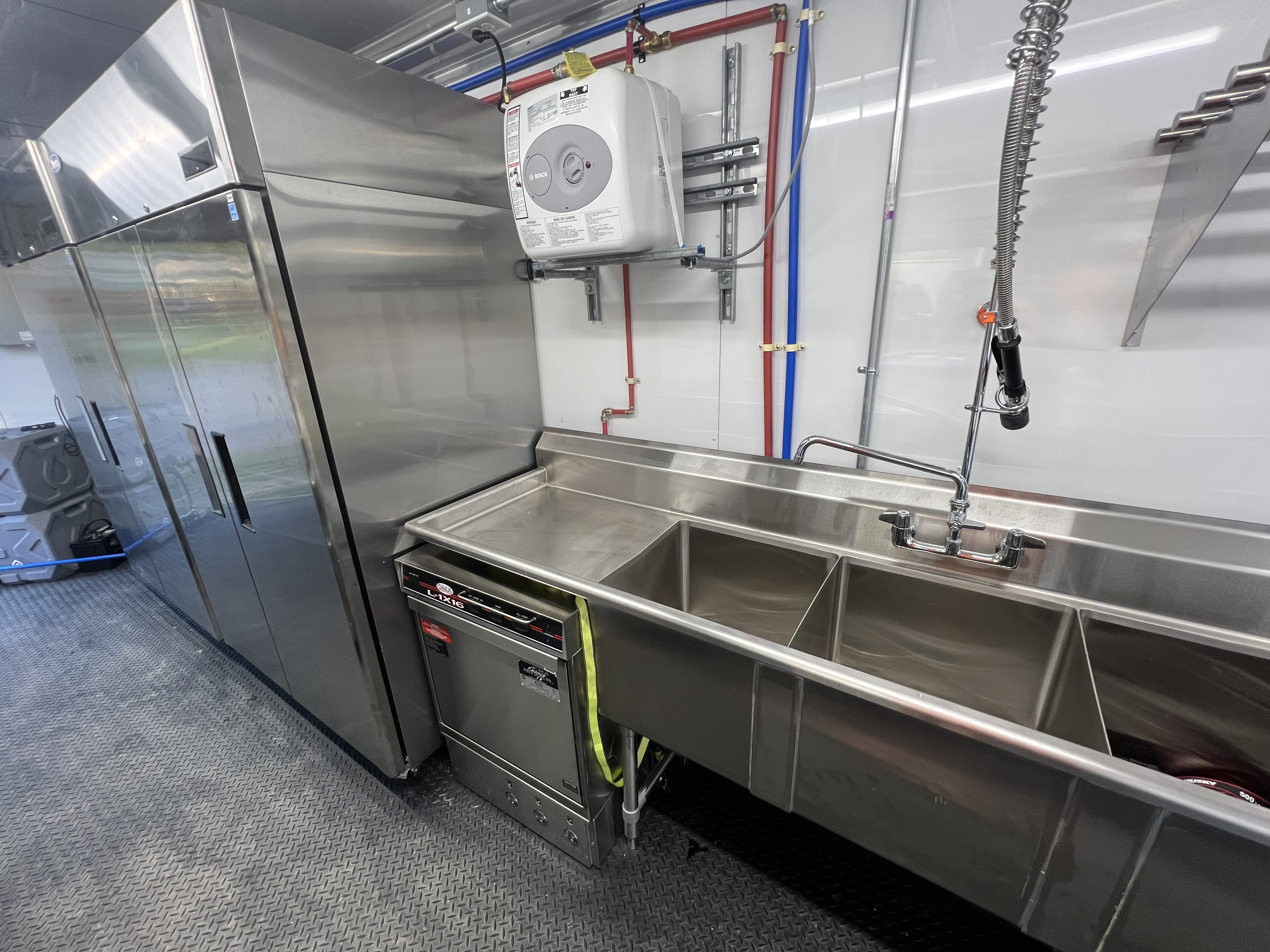 Interior view of the kitchen with triple sink, commercial dishwasher, and refrigerator units